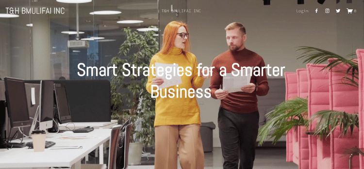 Two people, a woman with red hair and a man with a beard, walking and talking in a modern office environment with computer desks, plants, and pink seating.